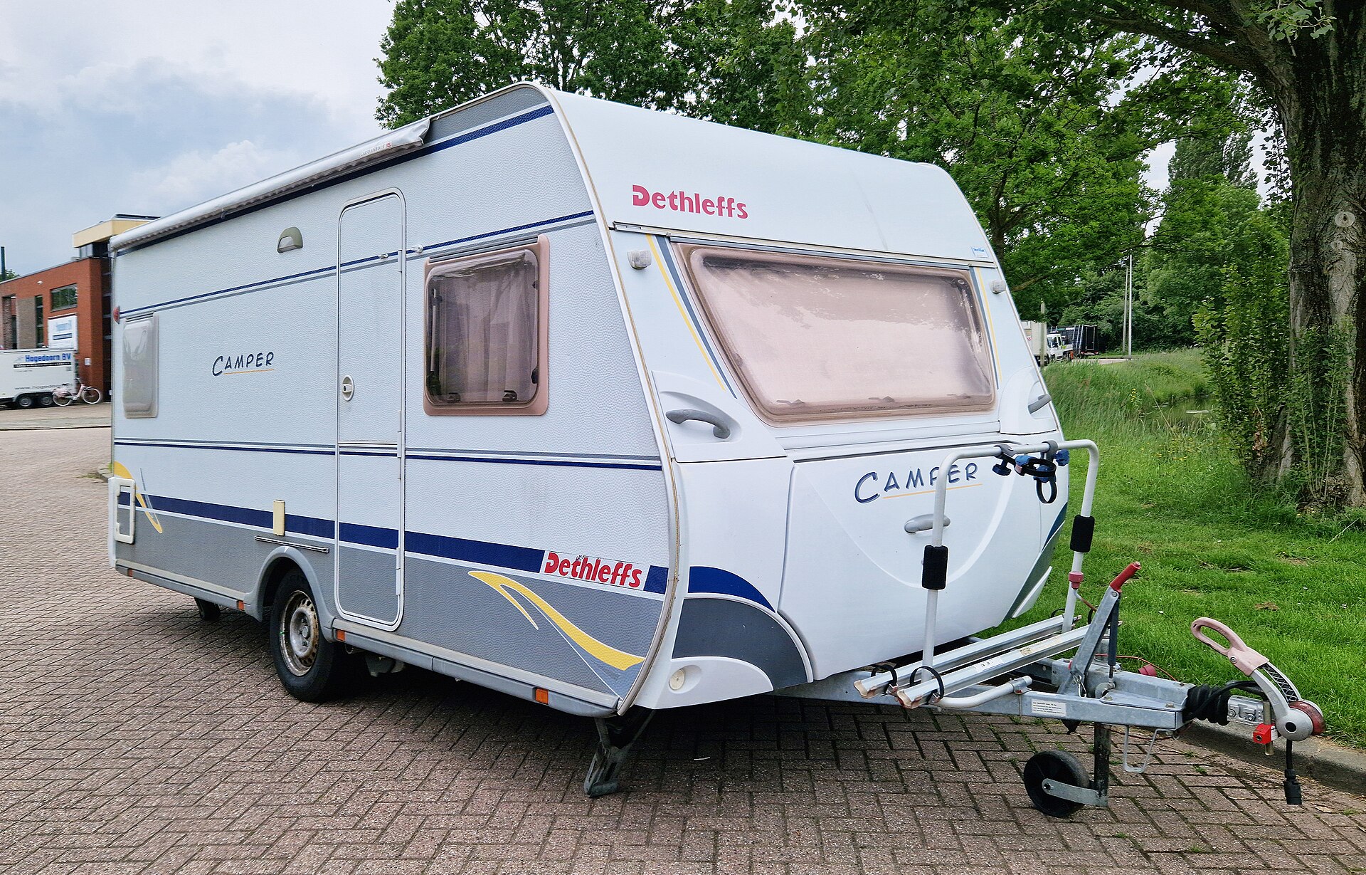 Een Europese Dethleffs-trekcaravan met een blauwe streep en zichtbare dissel staat op straat in Nederland.