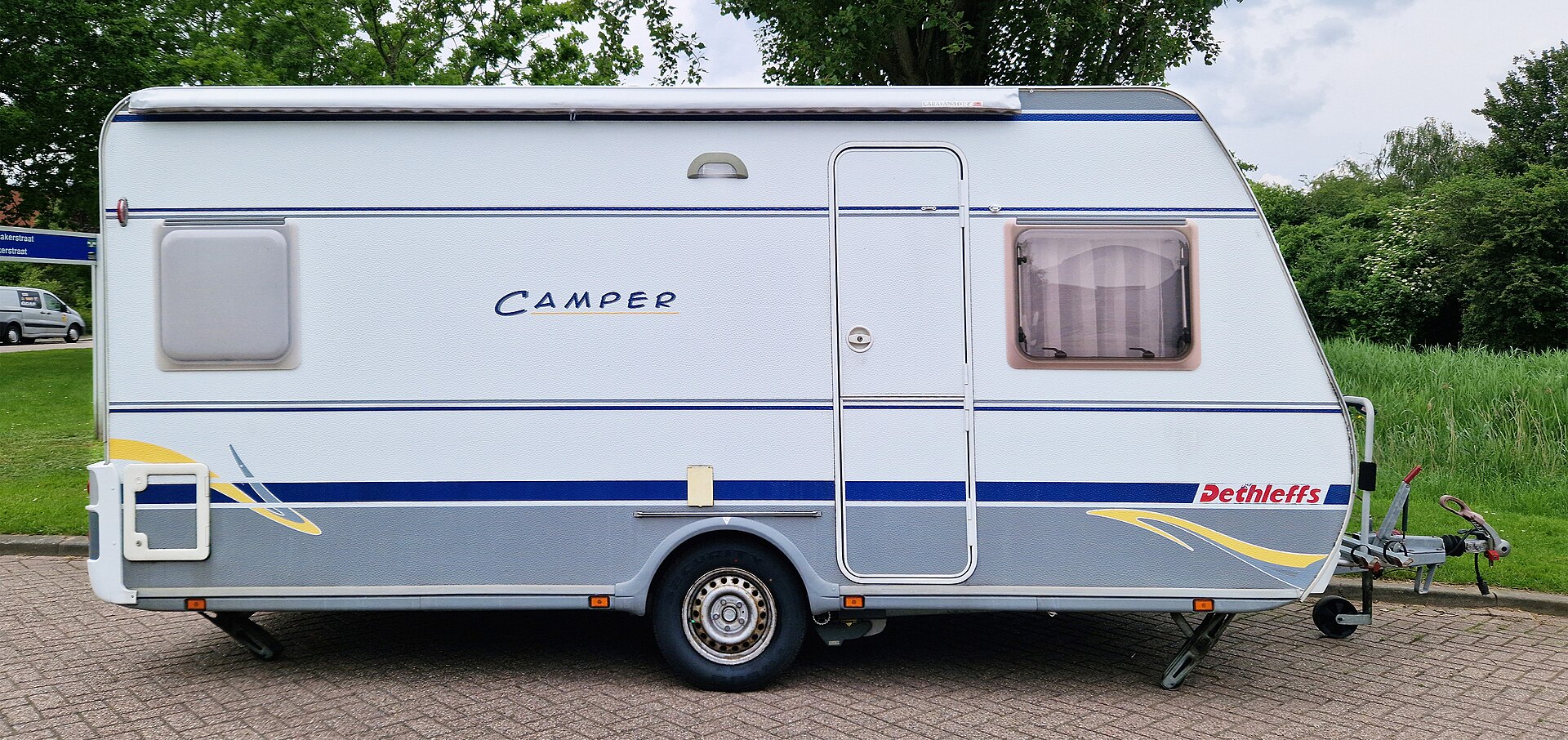 Zijaanzicht van een Dethleffs-trekcaravan met blauwe streep en een dissel aan de rechterkant.