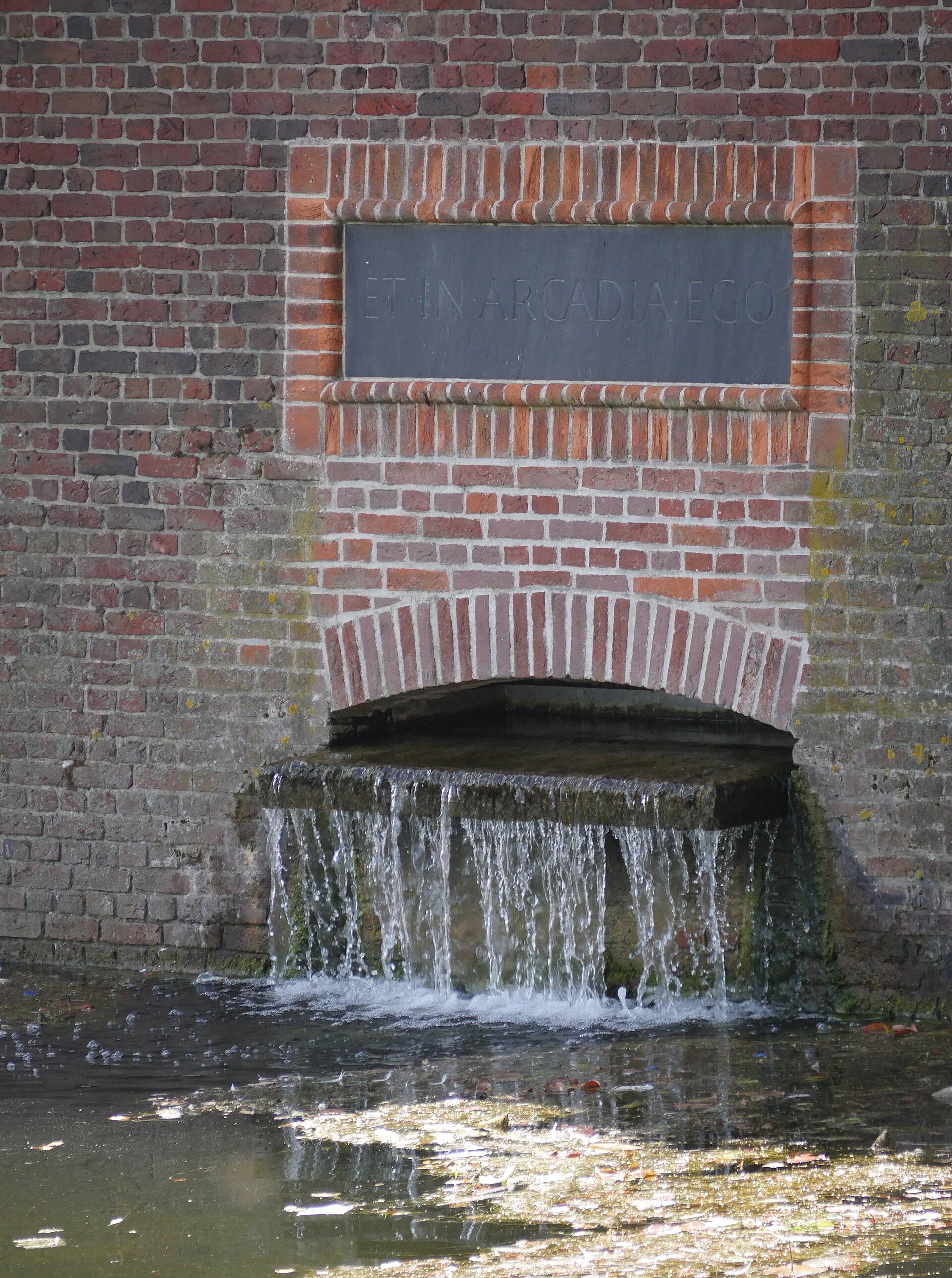 De gemetselde uitstroomopening van de Haagse Beek in de Hofvijver, met een Latijnse tekst en stromend water.