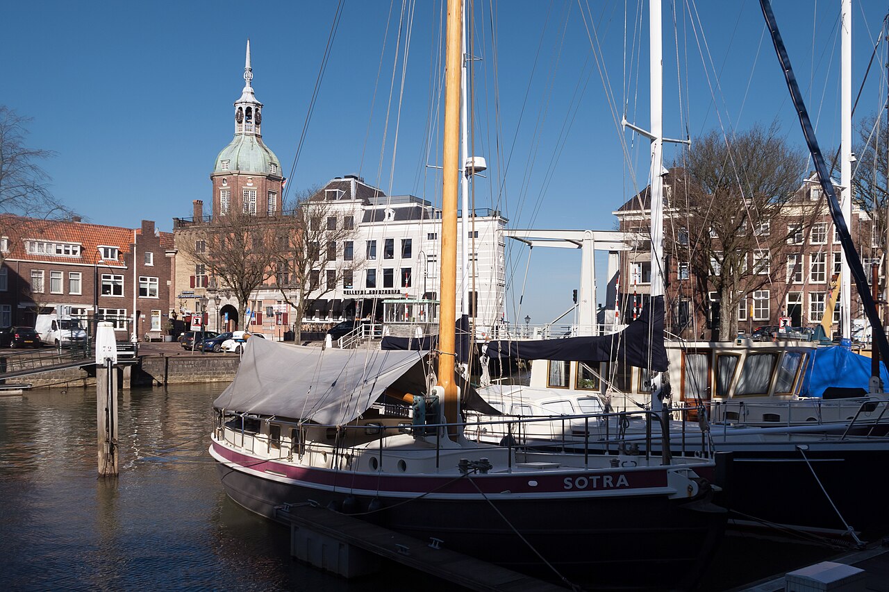 De Groothoofdspoort van Dordrecht achter aangemeerde schepen en een witte brug.