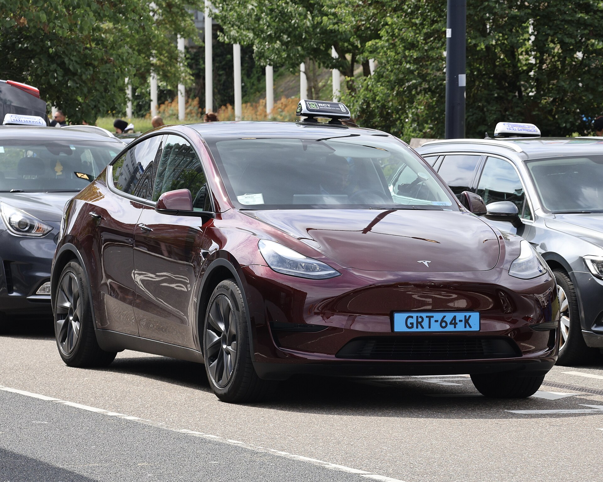 Een rode Tesla Model Y met Nederlands taxikenteken staat op een straat in Rotterdam.