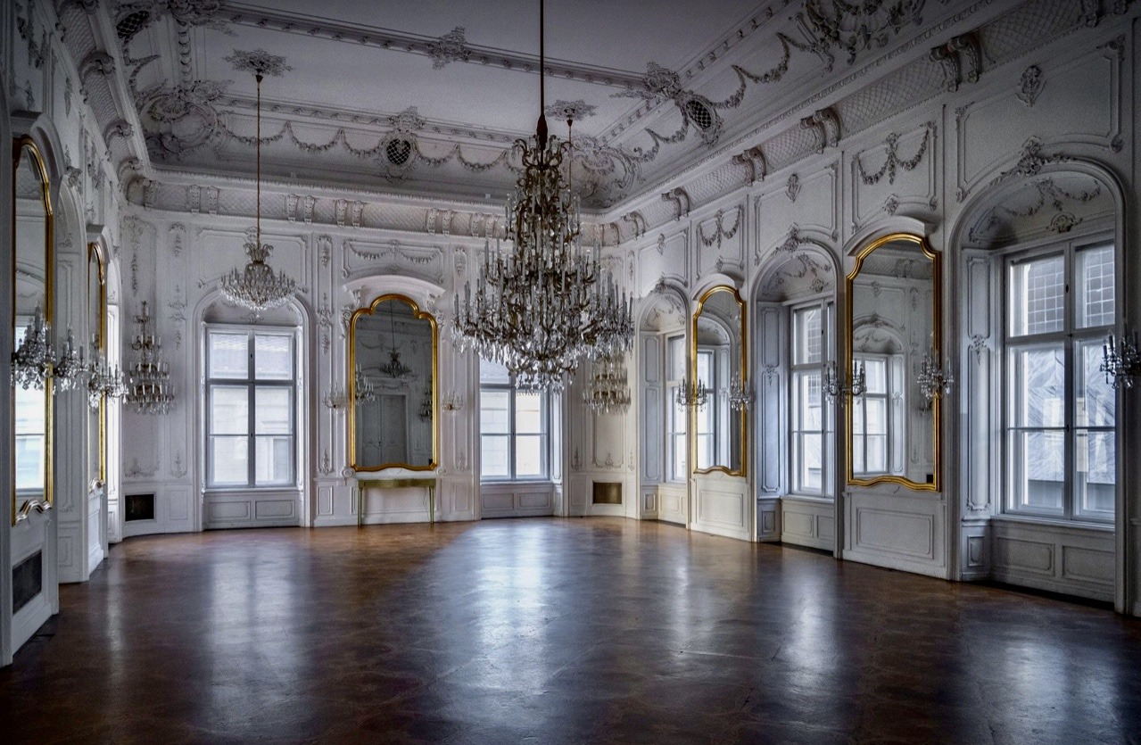 Een lege paleiszaal met grote spiegels en sierlijke plafonds.