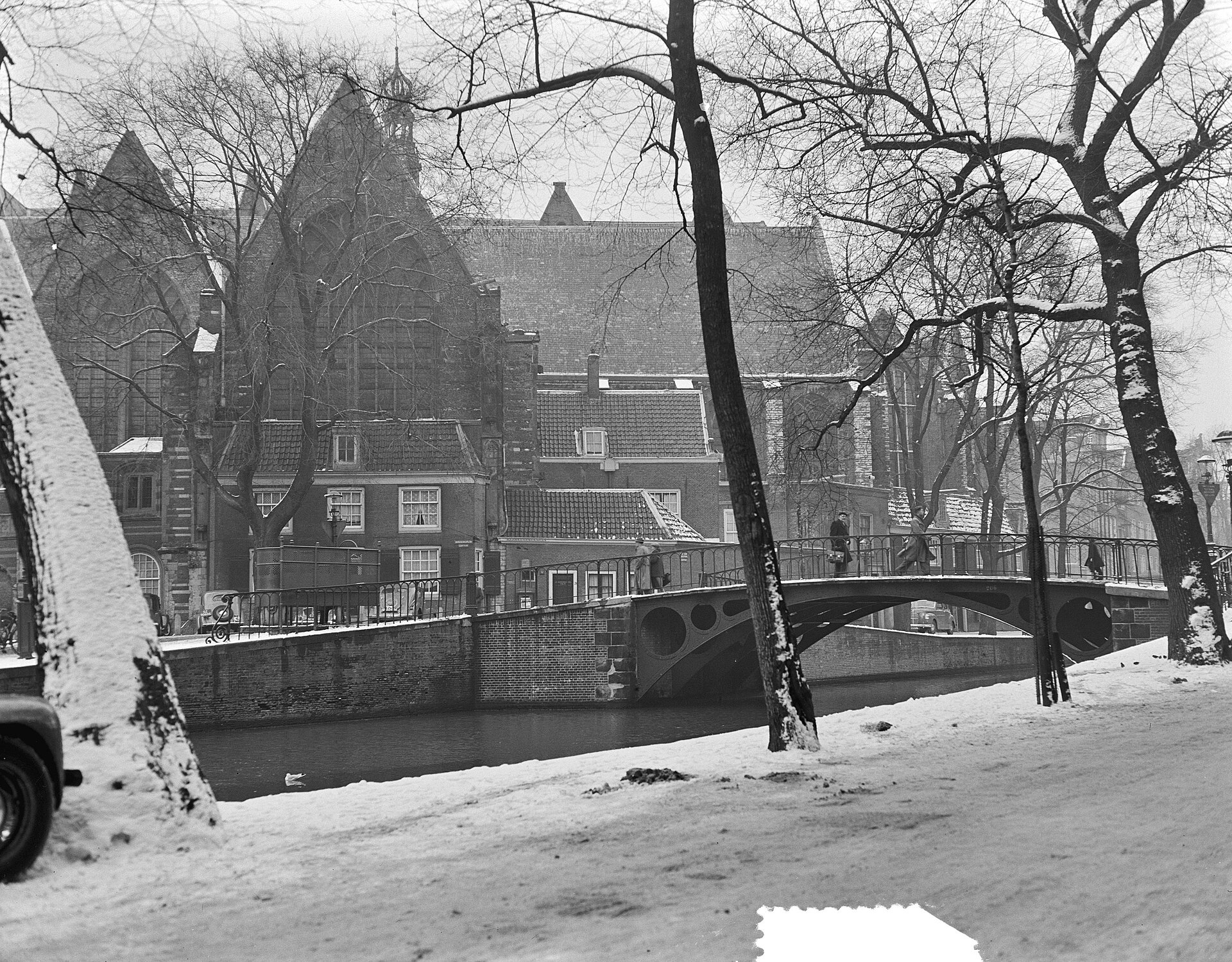 Besneeuwde Amsterdamse gracht en boogbrug op een zwart-witfoto uit 1952.