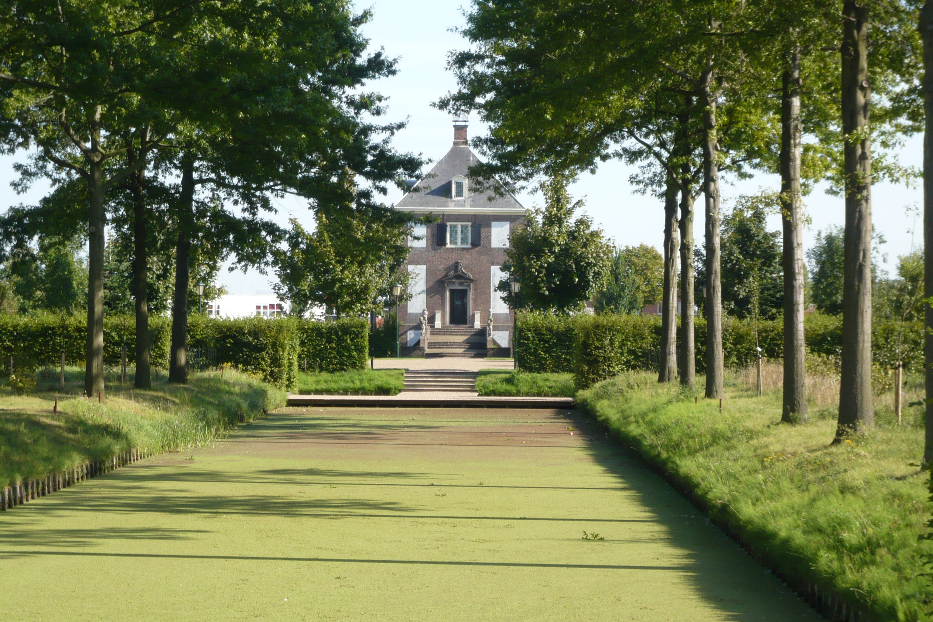 Huis Hofwijck aan het einde van een rechte waterpartij, tussen bomen en tuinpaden.