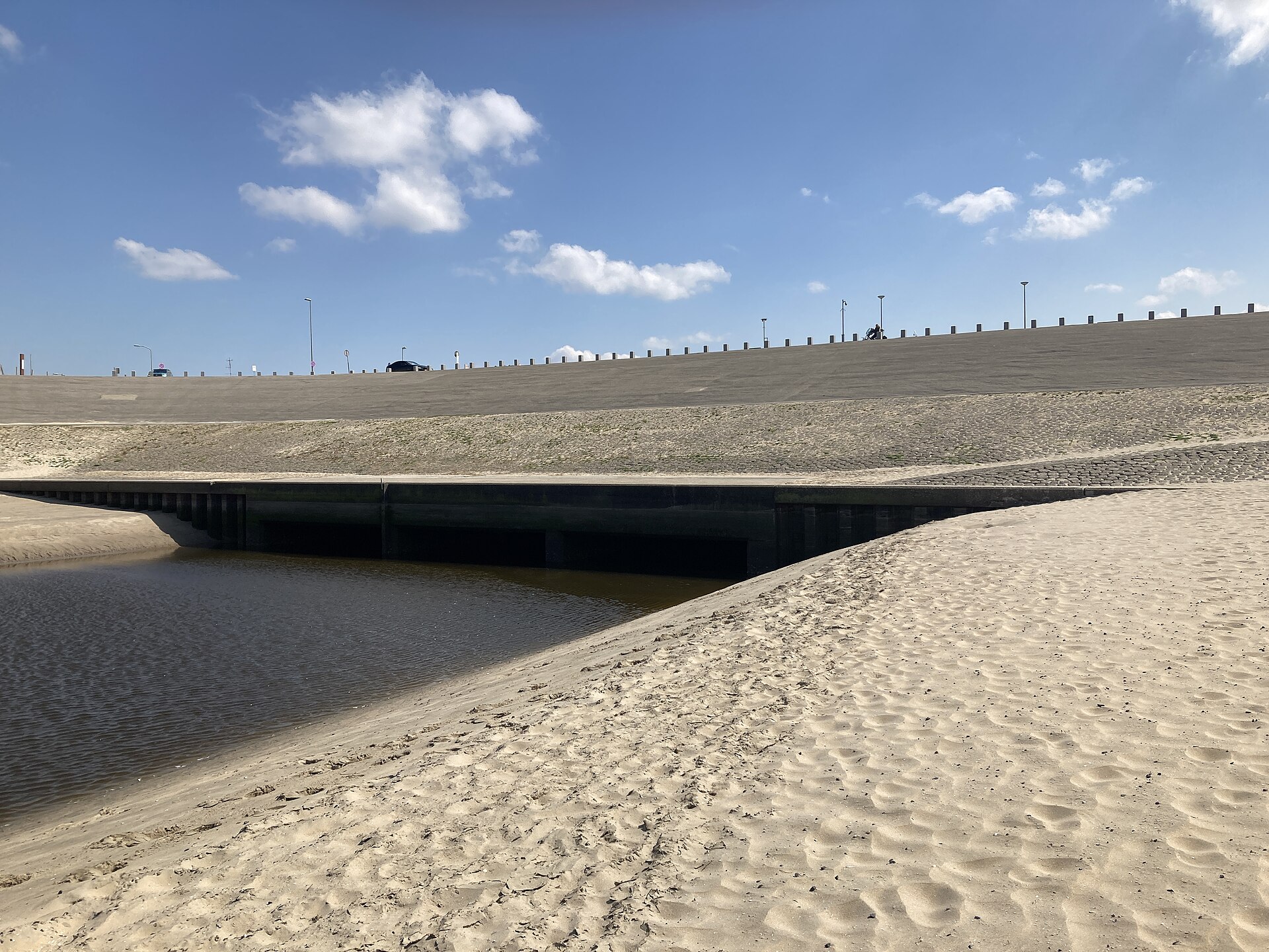 De Buitensluis bij Katwijk, gezien vanaf het zandstrand met water op de voorgrond.