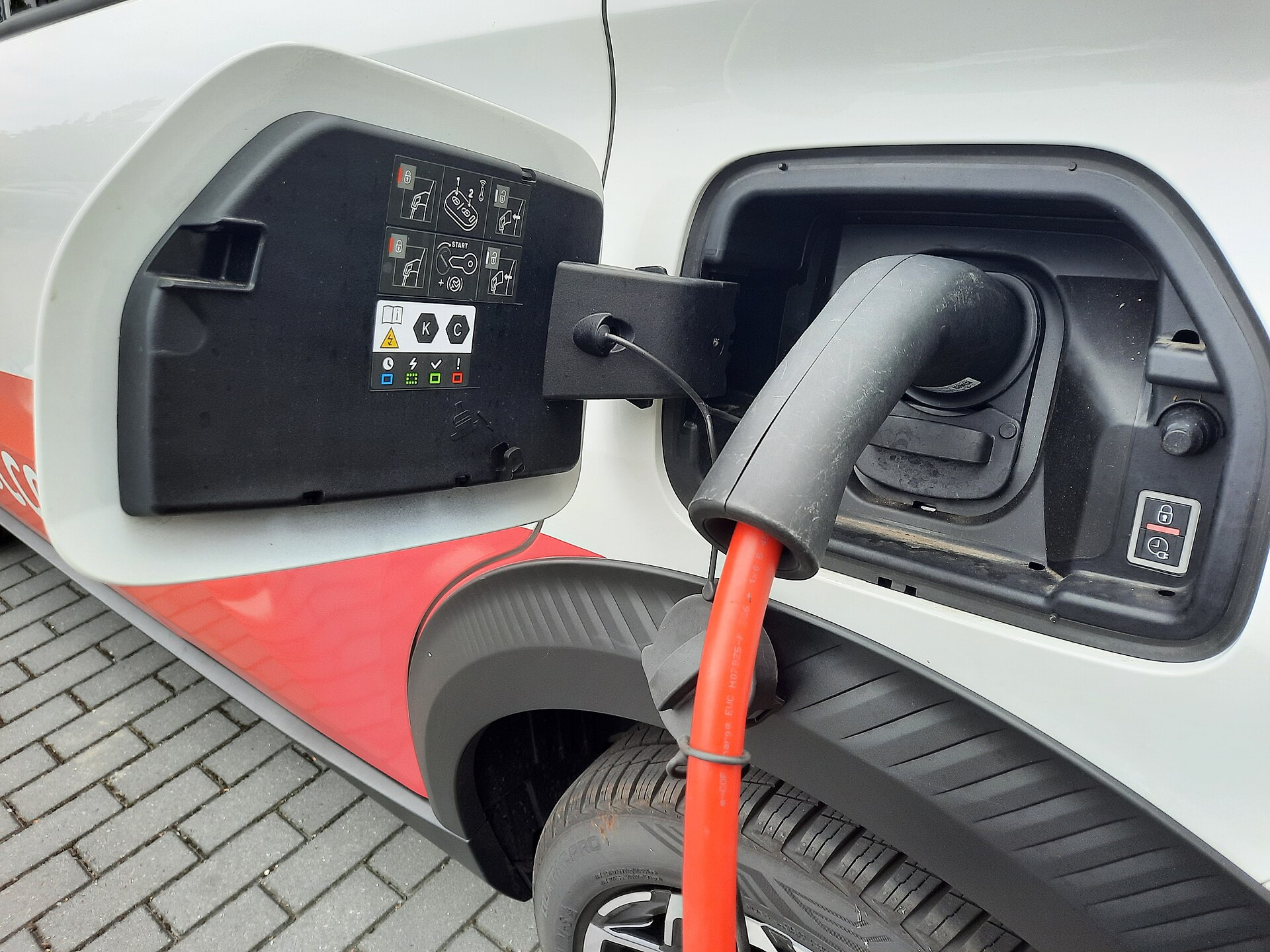 Een Type 2-laadstekker met oranje kabel zit in de geopende laadaansluiting van een auto.