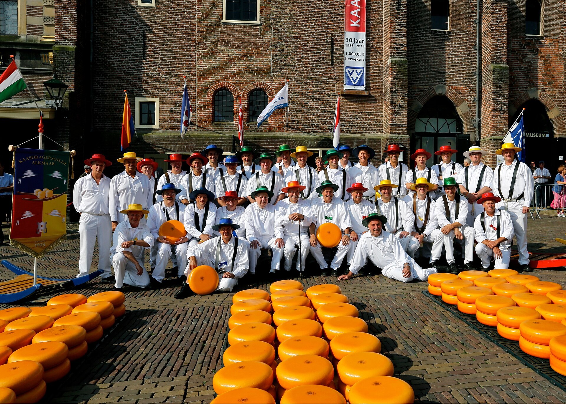 Het Alkmaarse kaasdragersgilde in 2013, met gekleurde hoeden en kazen op het plein.