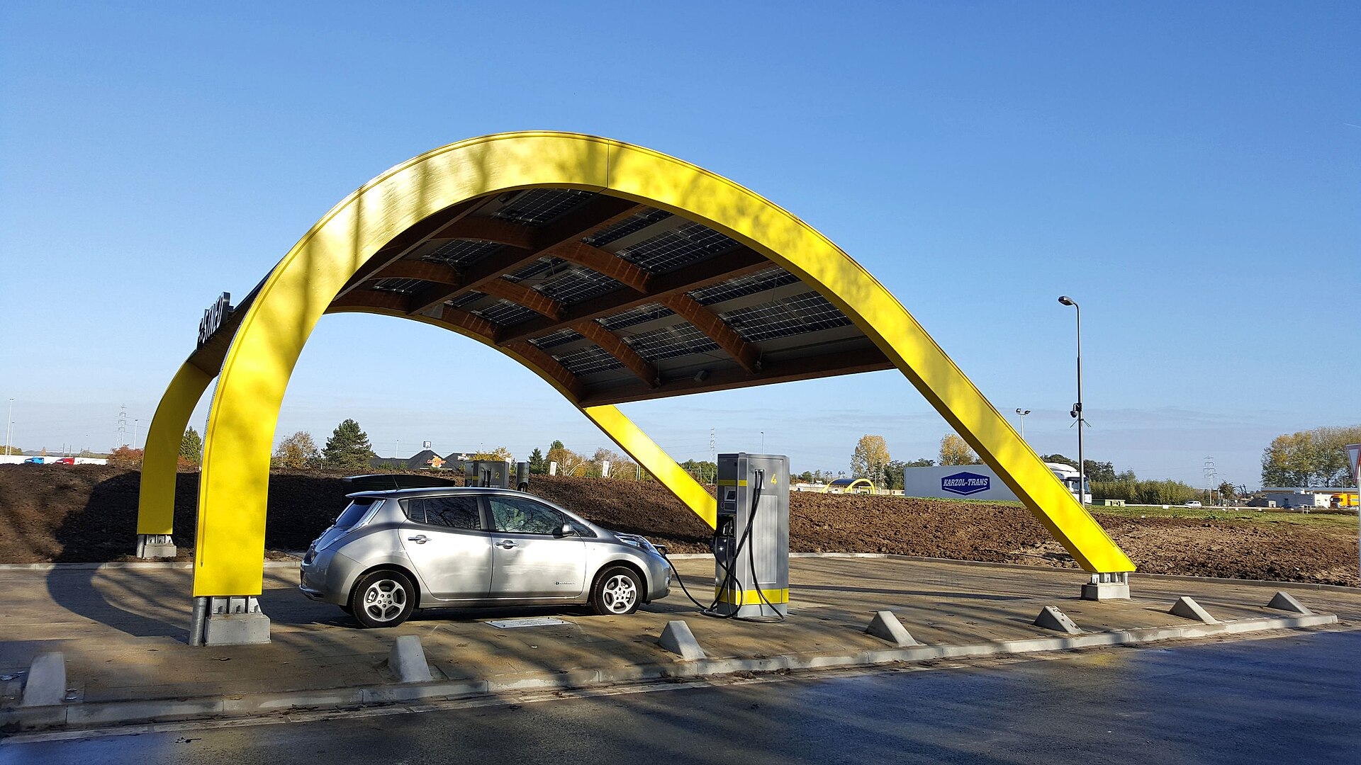 Een auto onder het gele zonnedak van een Fastned-laadstation.
