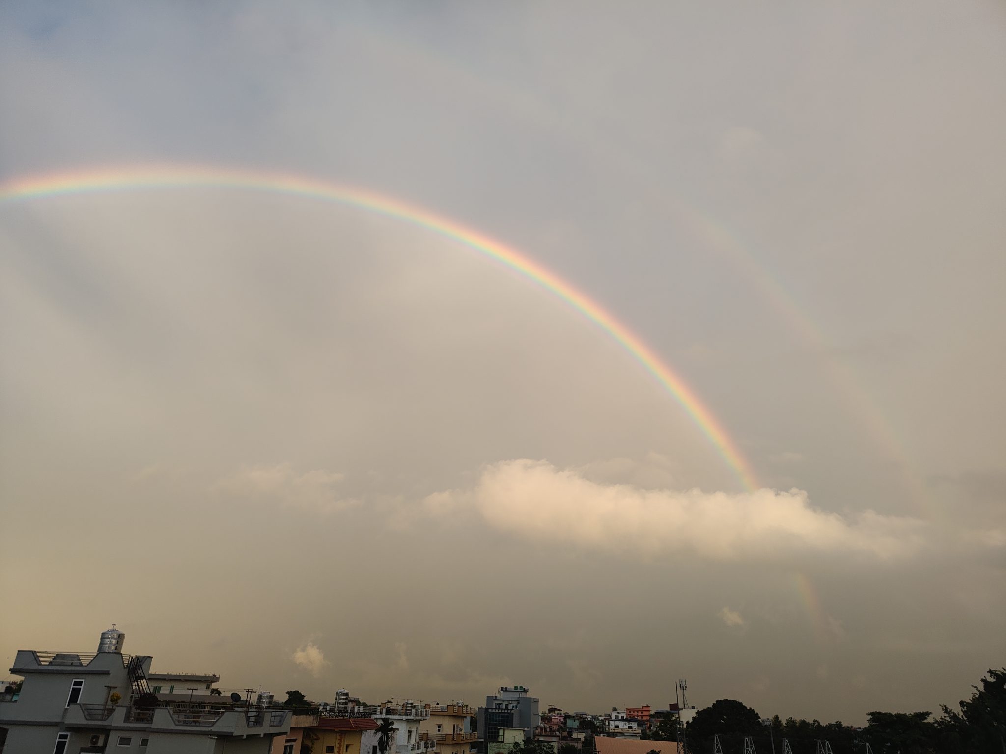 Een regenboogboog boven gebouwen onder een bewolkte hemel.