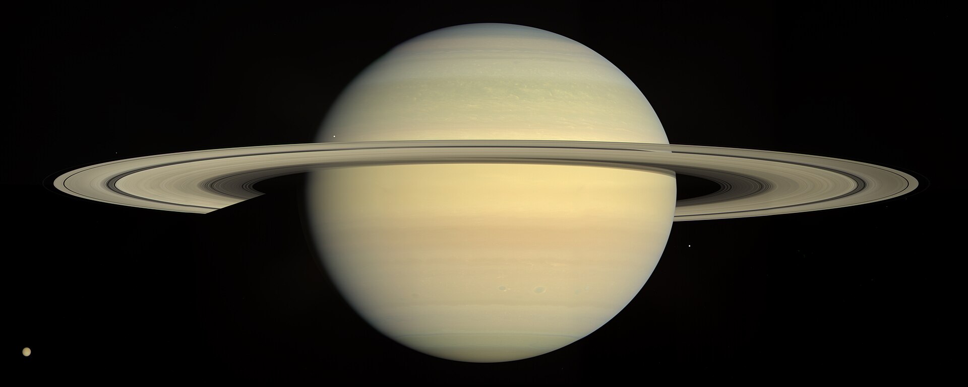 Saturnus met zijn brede ringen en enkele kleine manen tegen een zwarte achtergrond.