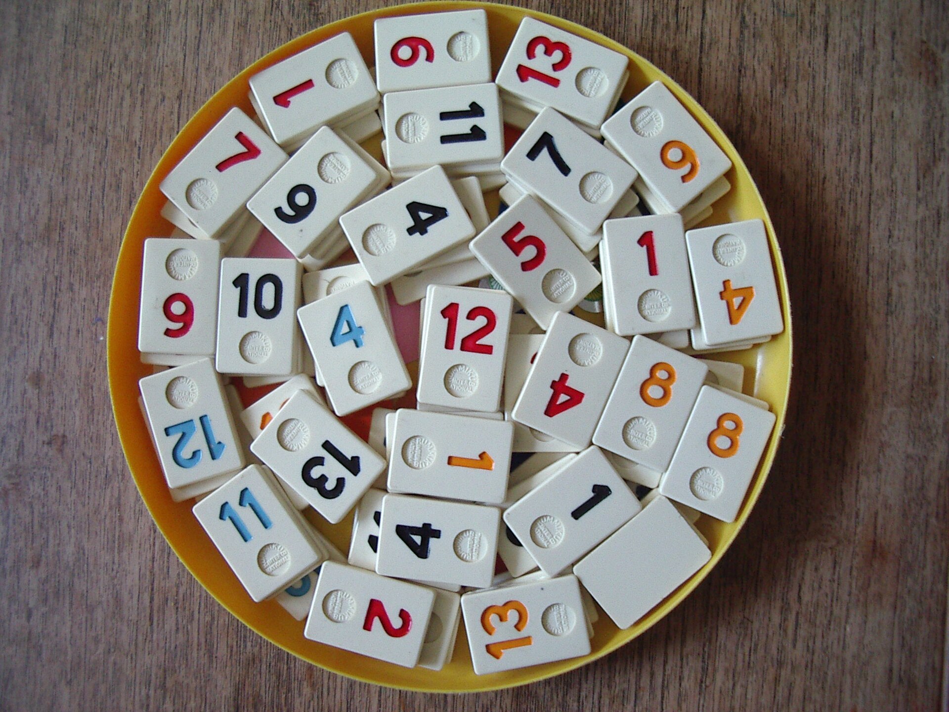 Rummikub-stenen met cijfers en een joker op een rond bord.