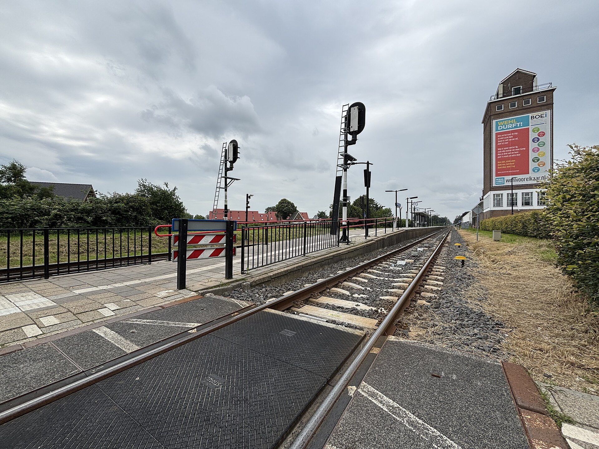 Twee spoorrails lopen langs het perron van station Wehl onder een bewolkte hemel.