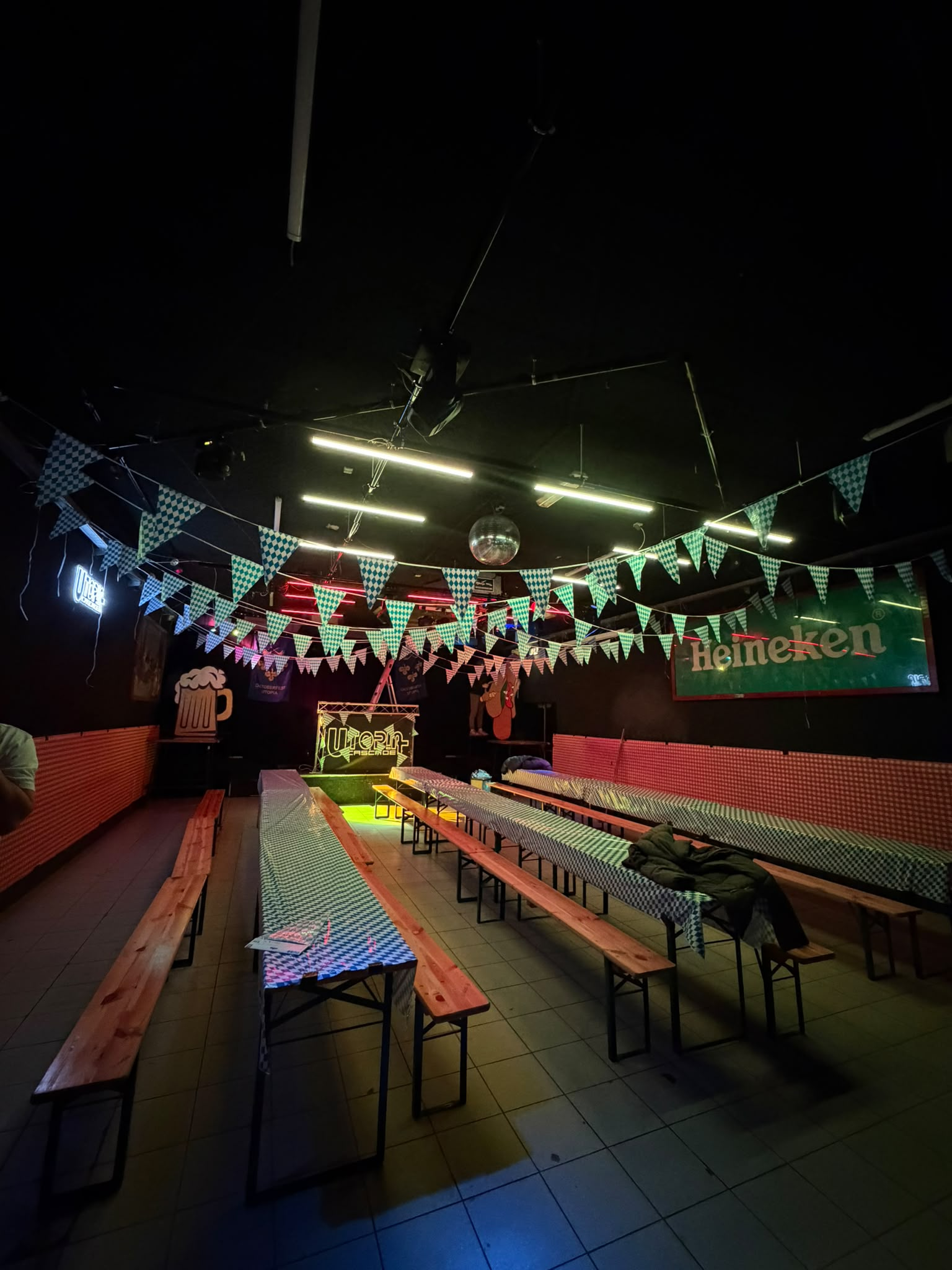 De zaal van Utopia met lange tafels, banken en geruite vlaggenslingers voor Oktoberfest.