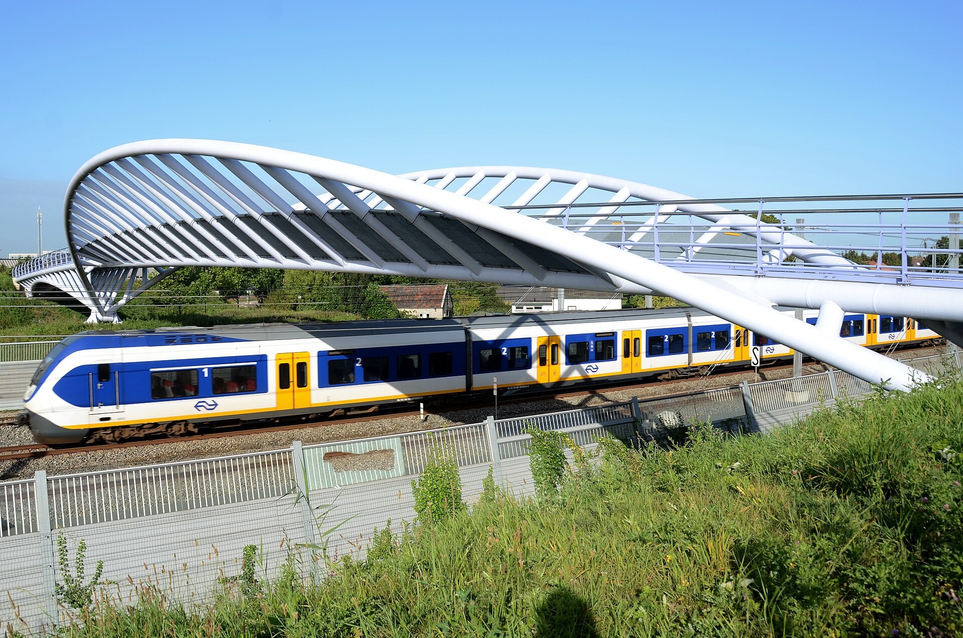 Een fiets- en voetgangersbrug over het spoor in Houten, met een trein eronder; illustratief beeld bij het verkeersnetwerk.