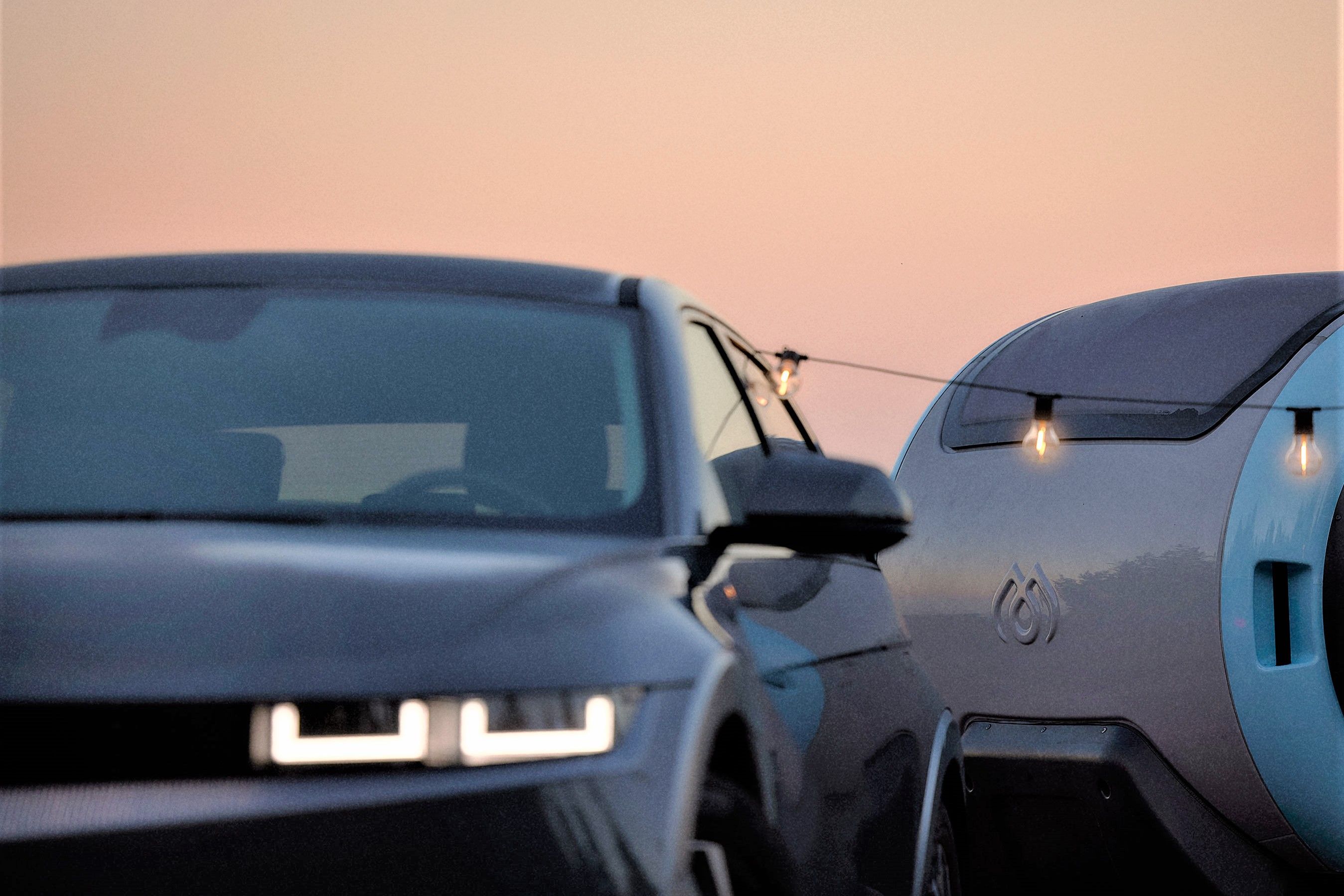 Een close-up van een Hyundai IONIQ 5 en MINK Camper met een lichtsnoer in de avond.