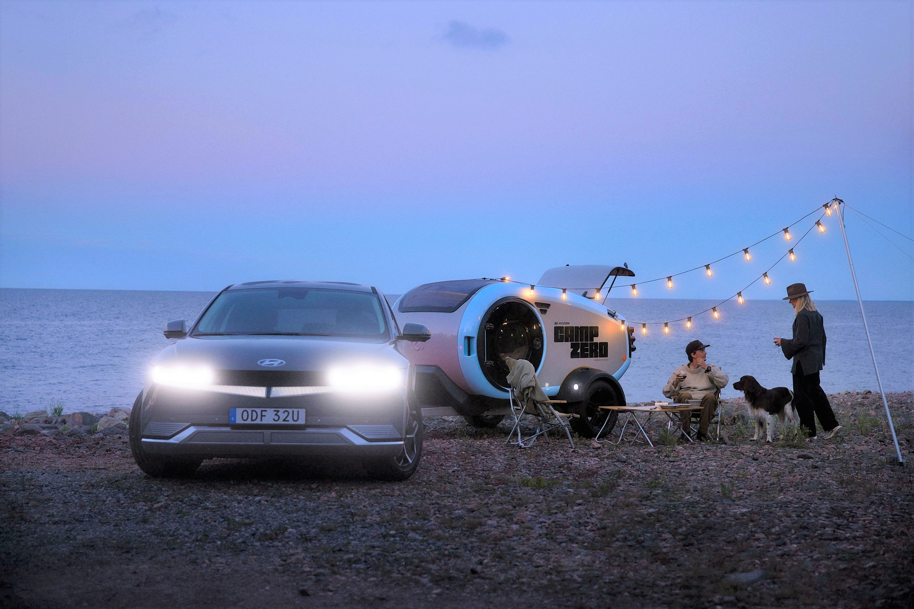 Een Hyundai IONIQ 5 met een kleine MINK Camper en kampeerders bij het water in de avond.