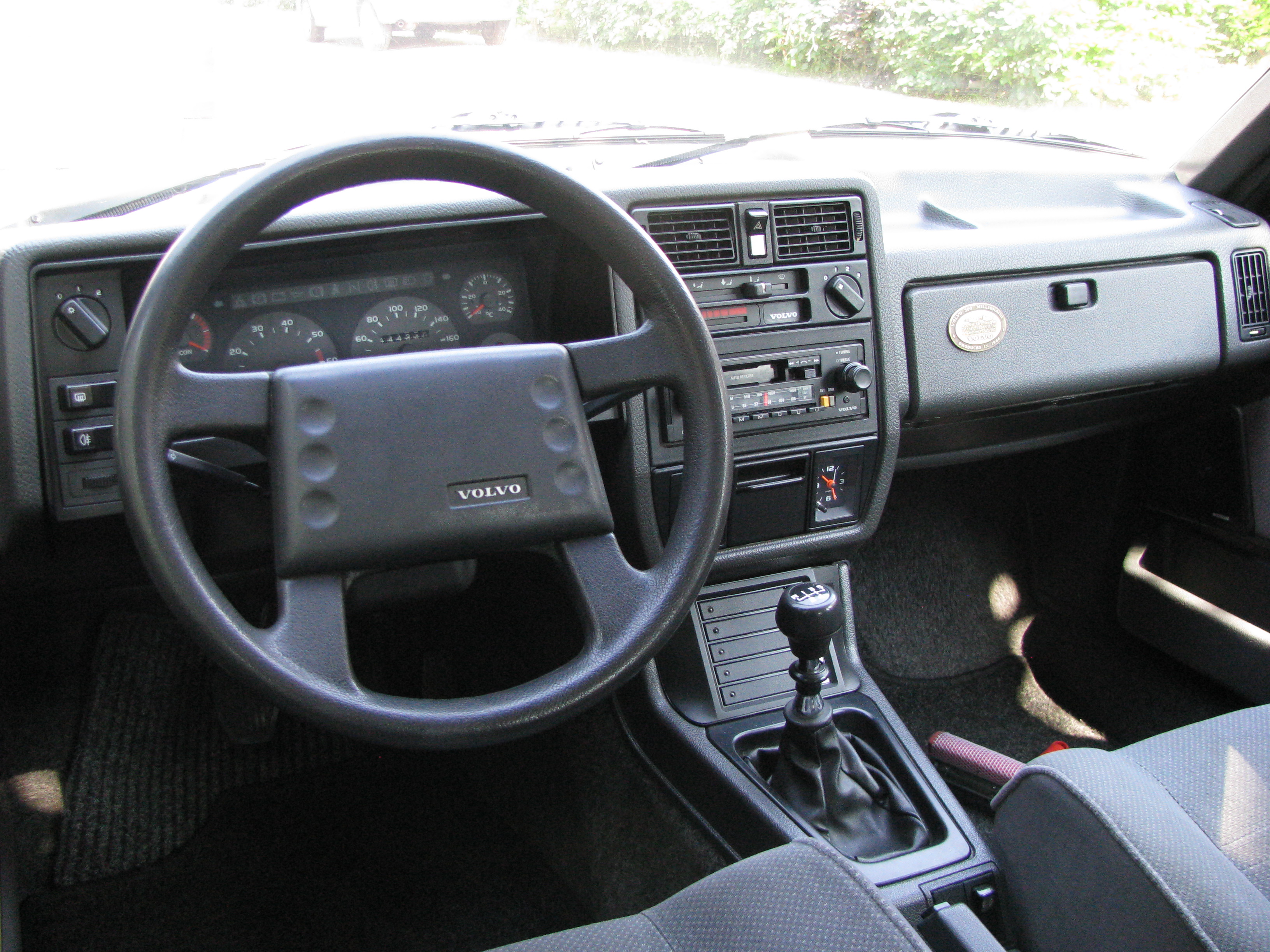 Dashboard van een Volvo 340 met analoge meters, cassetteradio en een versnellingspook met H-schema.