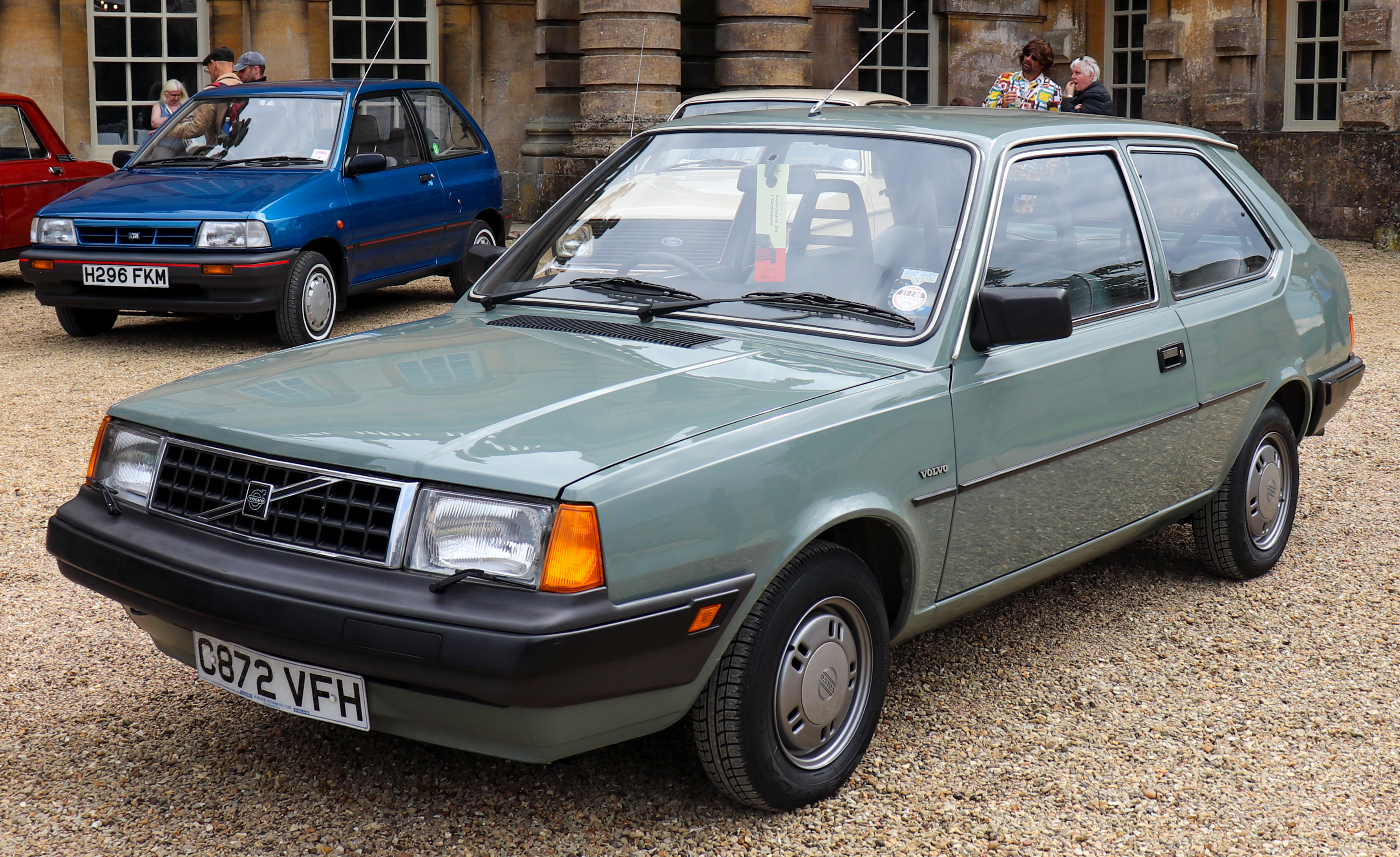 Een lichtgroene driedeurs Volvo 340 DL, schuin van voren gefotografeerd bij een autobijeenkomst.