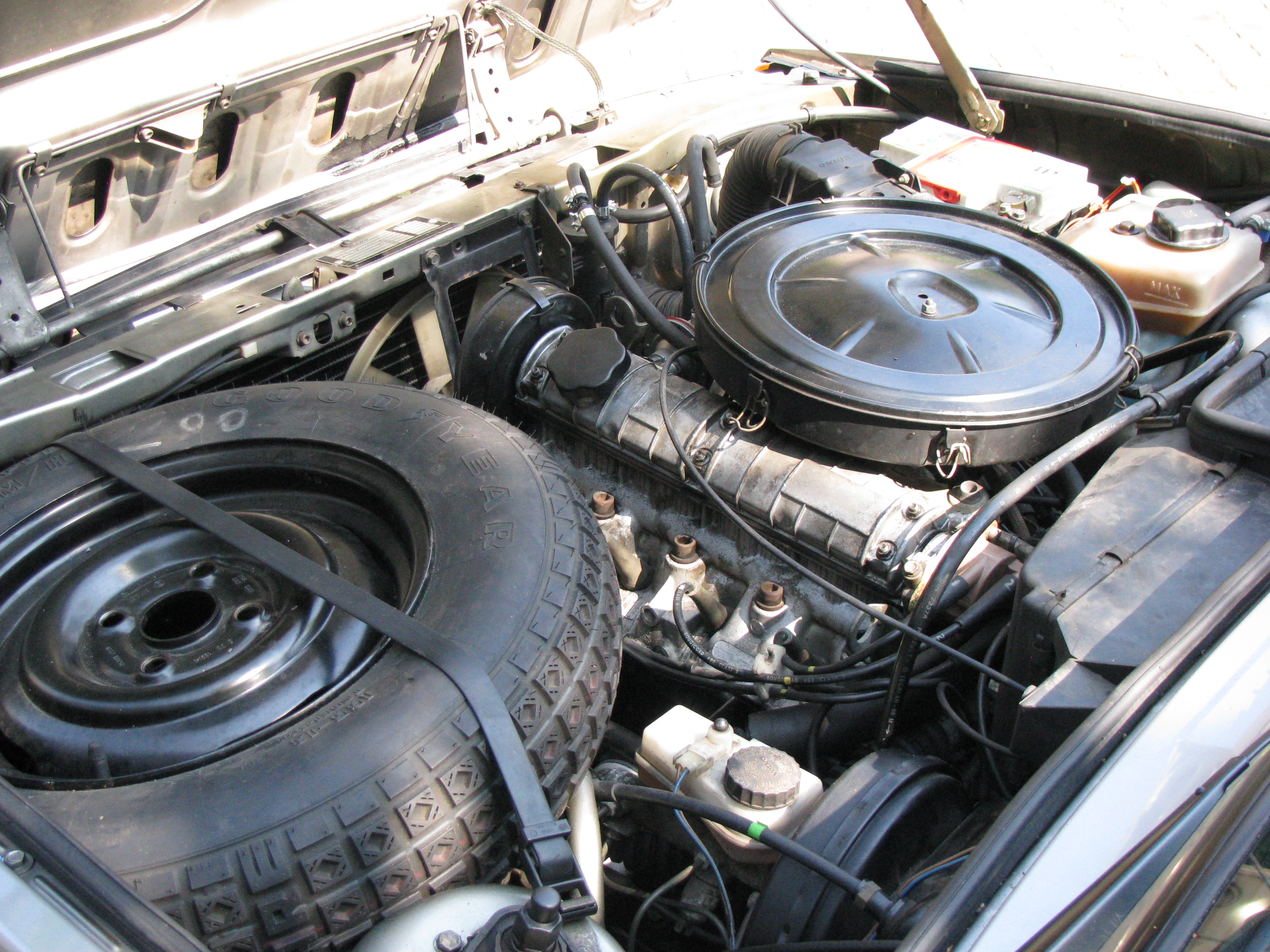Open motorruimte van een Volvo 340, met rond luchtfilterhuis en reservewiel naast de motor.