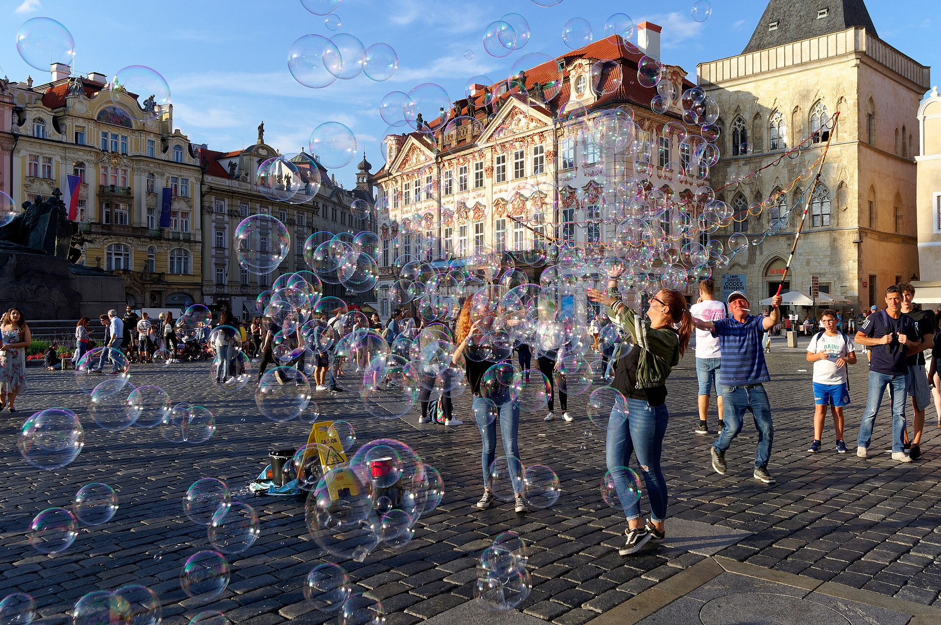 Grote doorzichtige zeepbellen zweven over een plein met historische gebouwen in Praag.