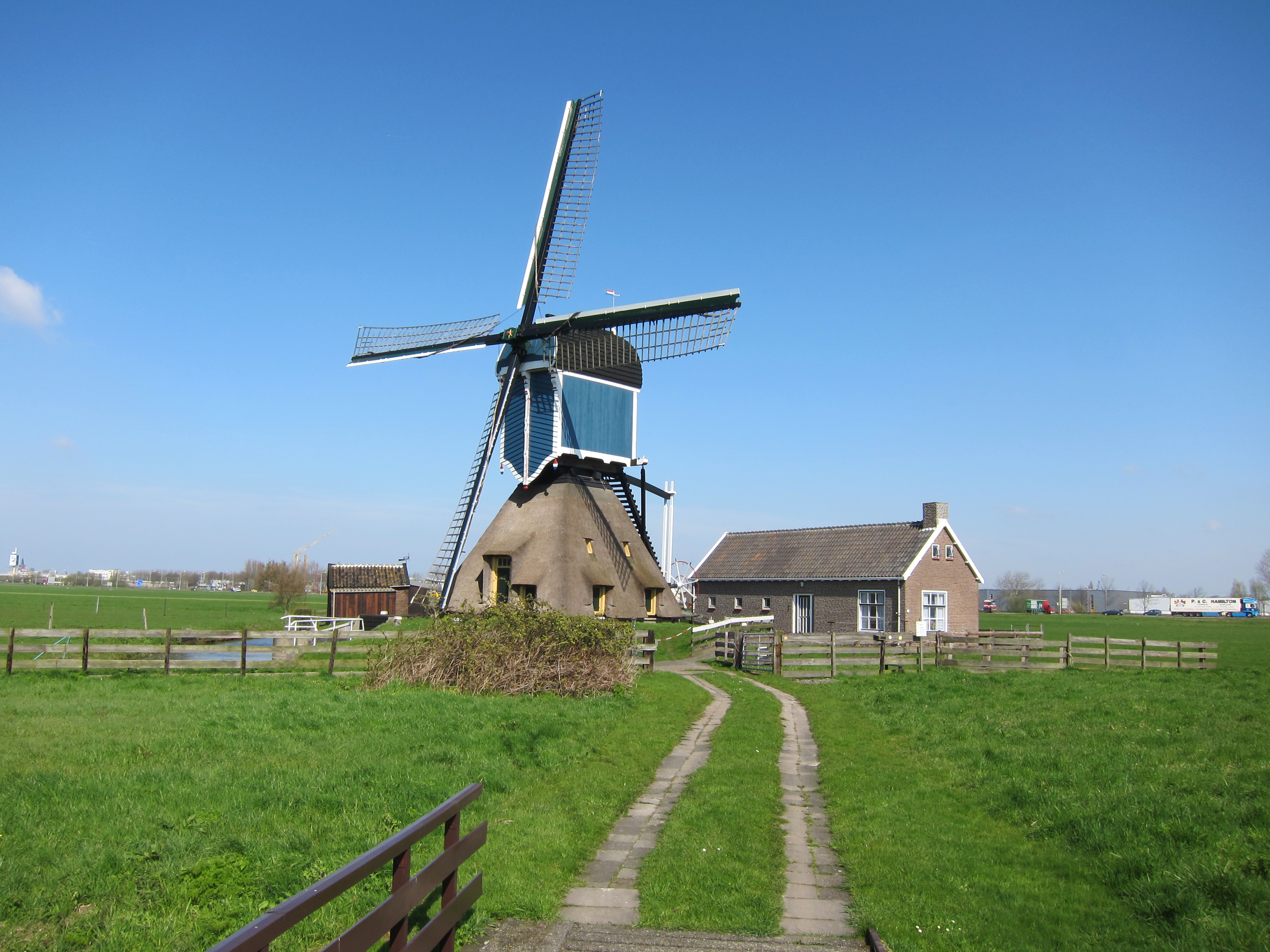 De Groote Molen in Zoeterwoude met grijsblauw bovenhuis, wieken en een paadje langs het water.